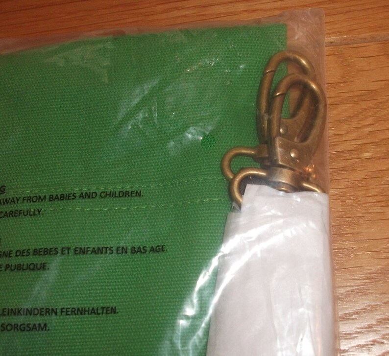 Puede incluir: Una bolsa de lona verde con un cierre de lat&oacute;n. La bolsa tiene una etiqueta de advertencia que dice: "Mantener fuera del alcance de beb&eacute;s y ni&ntilde;os. Manipular con cuidado."