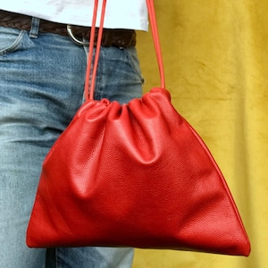 May include: A bright red leather drawstring bag with a gathered top and long red straps.