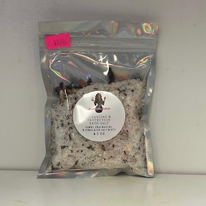 Może przedstawiać: Przezroczysta, zamykana torebka wypełniona solami do kąpieli. Okrągła naklejka z przodu głosi "Cleansing & Protection Bath Salt" z wymienionymi składnikami. Torebka zawiera 127.5 gramów produktu.