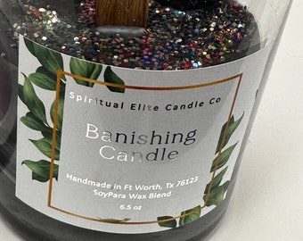 May include: A black soy candle with glitter and charcoal pieces inside. The label reads "Spiritual Elite Candle Co. Banishing Candle Handmade in Ft Worth, TX 76123 SoyPara Wax Blend 6.5 oz"