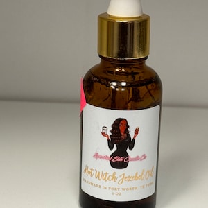 Puede incluir: Una botella de vidrio marrón con tapa dorada y gotero blanco. La botella está etiquetada con "Hot Witch Jezebel Oil" y "Handmade in Fort Worth, TX 76118". La etiqueta también presenta una ilustración de dibujos animados de una mujer con cabello negro largo que lleva un vestido negro y sostiene una vela.