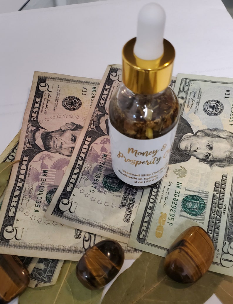 Peut inclure: Une bouteille en verre transparent avec un bouchon et un compte-gouttes dor&eacute;s remplie d'un liquide brun. La bouteille est &eacute;tiquet&eacute;e "Money & Prosperity" et est entour&eacute;e de billets de dollars am&eacute;ricains et de pierres &oelig;il de tigre.