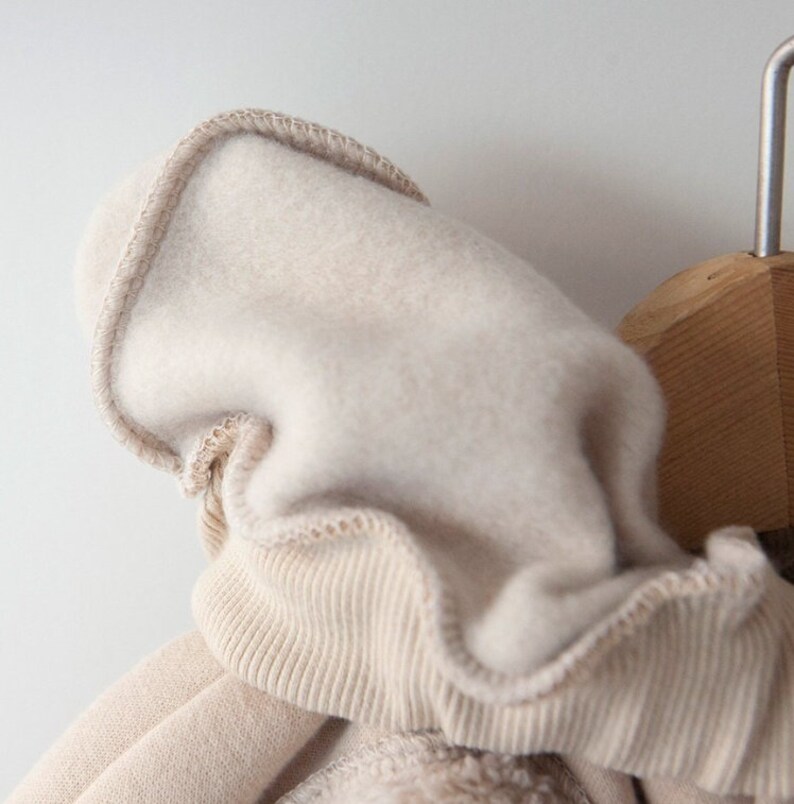May include: A beige hooded sweatshirt with a soft, fuzzy lining. The hood is folded down and the sweatshirt is hanging on a wooden hanger.