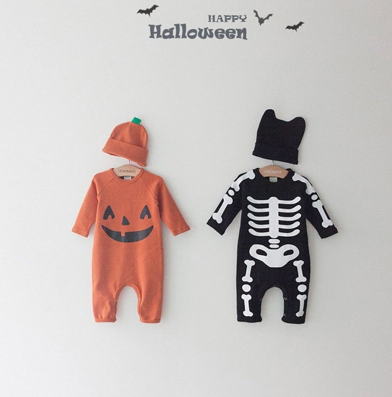 Op de afbeelding: Twee Halloween-babykostuums, een is een pompoen en de andere is een skelet. Beide kostuums zijn oranje en zwart met een bijpassende muts.