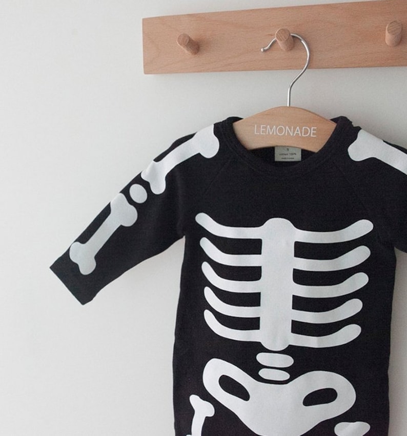 Op de afbeelding: Zwarte lange mouwen romper met een wit skelet ontwerp. De romper hangt aan een houten hanger met het woord "LEMONADE" erop gedrukt.