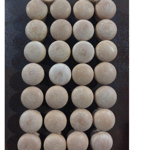 May include: A collection of twenty-eight unfinished light-colored wooden knobs arranged in a grid of four columns and seven rows. Each knob features a smooth, rounded top surface with visible natural wood grain patterns and a light beige tone.