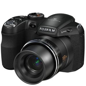 May include: A black Fujifilm FinePix S digital camera featuring an 18x wide optical zoom lens with a focal length of 5.0-90.0mm and an aperture of 1:3.1-5.6. The camera body includes a top-mounted mode dial, a shutter button, and a flash release.