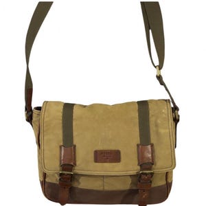 May include: A tan canvas messenger bag with a dark brown leather base and trim. The bag features two vertical olive green fabric straps with brown leather buckles, a long adjustable olive green shoulder strap, and a brown leather Fossil brand patch.