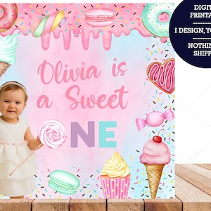 May include: A pink and blue printable backdrop for a first birthday party with a sweet theme. The backdrop features a girl in a white dress, a donut, ice cream cones, cupcakes, candy, and the text "Olivia is a Sweet ONE".