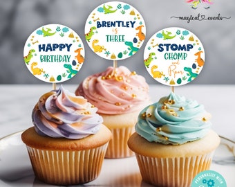 May include: Three cupcakes with colorful frosting and decorative toppers. The toppers feature dinosaur illustrations and text that reads "Happy Birthday", "Brentley is Three", and "Stomp Chomp and Roar". Gold sprinkles adorn the frosting.