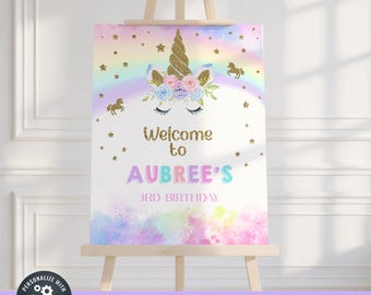 May include: A party sign on an easel features a unicorn design with a gold horn, floral accents, and a rainbow. The sign reads "Welcome to AUBREE'S 3RD BIRTHDAY" in colorful text, with gold stars and unicorn silhouettes.