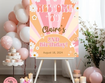 May include: A pink and orange welcome sign with a retro 70s style font. The sign says "Welcome to Claire's 2nd Birthday! August 18, 2024". The sign is decorated with daisies, peace signs, and smiley faces.