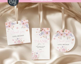 May include: Three baby shower gift tags with floral designs and the text "Thank you." The tags are white with pink and purple flowers and butterflies. Each tag has a ribbon for hanging. The text "Love, Meghan" is also visible.