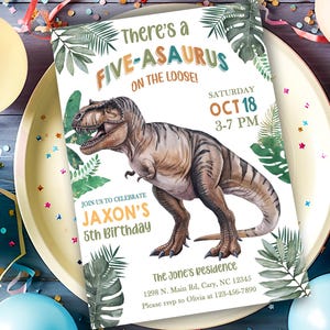 Op de afbeelding: Een dinosaurus-thema verjaardagsuitnodiging met de tekst "There's a FIVE-ASAURUS ON THE LOOSE!" en "Jaxon's 5th Birthday". De uitnodiging toont een illustratie van een Tyrannosaurus Rex en tropische bladeren. De uitnodiging ligt op een bord met ballonnen.