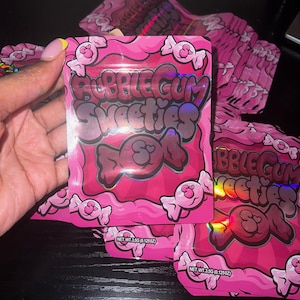 Pu&ograve; includere: Confezione rosa a tema bubblegum con la scritta "Bubblegum Sweeties DOA" e illustrazioni di caramelle. La confezione ha una lucentezza olografica e contiene 3,5 g di prodotto. Sono visibili diverse confezioni.