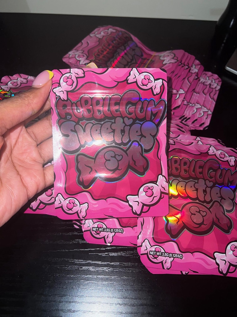 Pu&ograve; includere: Confezione rosa a tema bubblegum con la scritta "Bubblegum Sweeties DOA" e illustrazioni di caramelle. La confezione ha una lucentezza olografica e contiene 3,5 g di prodotto. Sono visibili diverse confezioni.