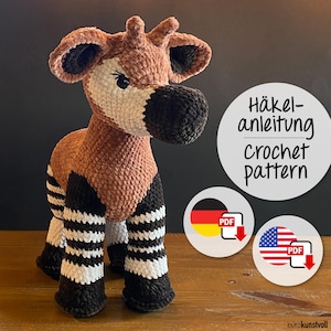May include: A plush, crocheted okapi toy in shades of brown, black, and white. The okapi has a long neck, large ears, and striped legs. The image includes a circular graphic with the text "Häkelanleitung crochet pattern" and a PDF download icon.