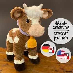 Puede incluir: Patrón de crochet para una vaca marrón y blanca con una campana amarilla. El patrón está disponible en descargas PDF en alemán e inglés.