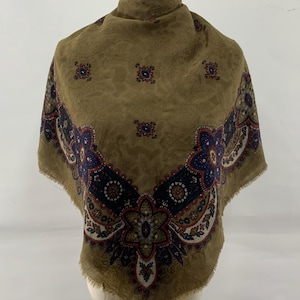 May include: Olive green scarf with a paisley pattern and a decorative border in navy, red, and cream. The scarf is displayed on a mannequin and has a fringed edge. The overall design is vintage.