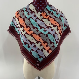 May include: A square scarf in deep burgundy featuring a repeating geometric pattern of stylized shapes in orange, light blue, and lavender. The neck area has a purple polka dot print, and the edges are finished with a fringe. The Bally logo is visible.