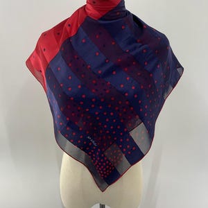 May include: A square silk scarf featuring a bold diagonal split design. One section is solid red with small dark polka dots, while the other is navy blue with red polka dots and stripes. The text jun ashida is printed in the lower corner.