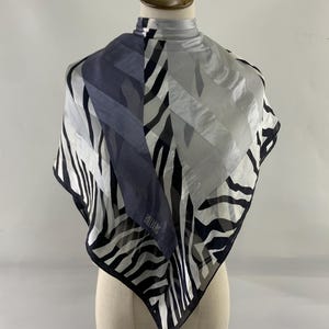 May include: A square scarf with a zebra stripe pattern in black and white, with a section of solid navy blue and grey. The scarf is draped over a mannequin. The brand name "BILL BLASS" is visible.