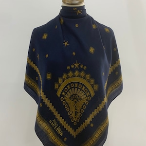 Puede incluir: Un pañuelo azul marino con un diseño dorado que presenta un símbolo alado, estrellas y el texto "Jean Paul GAULTIER".