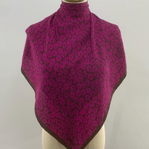 Puede incluir: Un pañuelo de seda con estampado rosa y marrón con borde marrón. El pañuelo se muestra en un maniquí blanco.
