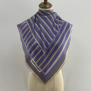 Puede incluir: Un pañuelo de seda beige con rayas azules y negras. El pañuelo tiene el texto "Dessins Charlet" impreso.