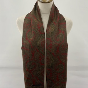 Pode incluir: Lenço com padrão paisley em tons de vermelho e castanho, exposto num manequim. O lenço apresenta um design intrincado com uma borda com franjas. A estética geral é clássica e elegante, adequada para várias ocasiões.