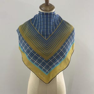 Puede incluir: Un pañuelo azul y dorado con un estampado de cuadros y rayas, expuesto sobre un maniquí. El pañuelo presenta una combinación de colores azul, blanco y dorado. El pañuelo tiene el texto "David Lewis" en la esquina inferior.