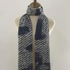 May include: A white and navy blue patterned scarf with a fringed edge.