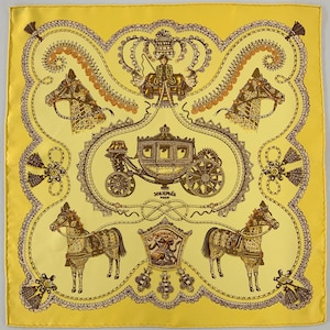 May include: Yellow silk scarf with a detailed equestrian design. The scarf features a central carriage illustration, horses, and decorative borders in shades of brown and gold. The scarf is square in shape.