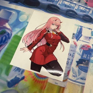 May include: A pink-haired anime character with red eyes wearing a red and black outfit. She is holding a green object in her right hand and has a serious expression on her face.