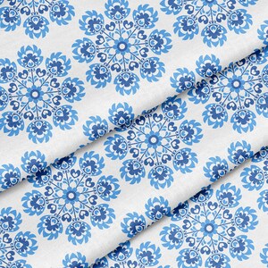Peut inclure: Tissu blanc avec un motif répétitif de motifs floraux bleus. Le motif présente des fleurs et des feuilles stylisées dans des tons de bleu clair et foncé. Le tissu est plié, montrant le motif sous différents angles.