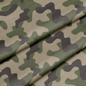 May include: Close-up of a camouflage fabric with a green, brown, and beige pattern. The fabric is folded in a way that shows the texture and detail of the pattern.