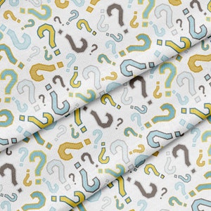 Puede incluir: Una tela blanca con un patrón repetitivo de signos de interrogación azules, amarillos y grises. La tela está doblada en tres partes, creando un efecto de capas.