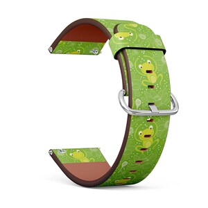 May include: A green watch strap featuring a repeating pattern of cartoon frogs and white floral designs. The strap has a brown leather backing and a silver buckle. The watch strap is designed to fit a standard watch.