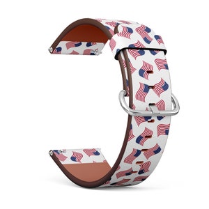May include: A white watch band with a repeating pattern of American flags in red, white, and blue. The band has a brown leather backing and a silver-colored buckle. The watch band is designed to fit a standard watch.