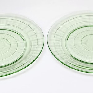 May include: Two round, light green glass plates featuring a central circular design surrounded by a series of radiating lines and a wide, smooth outer rim. The translucent plates have a uniform pale green tint and a polished finish.