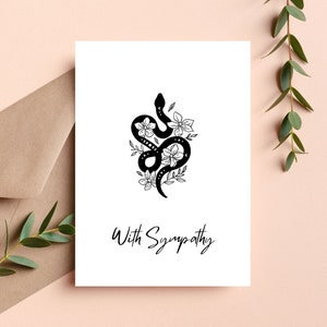 May include: A black and white sympathy card with a floral design featuring a snake wrapped around the flowers. The text "With Sympathy" is printed below the design.
