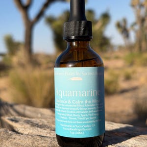 May include: A brown glass bottle with a black dropper, labeled "Aquamarine." The label is light blue with white text, listing benefits and ingredients. The bottle contains 1 fl oz (30ML) of liquid. The background is a blurred desert landscape.