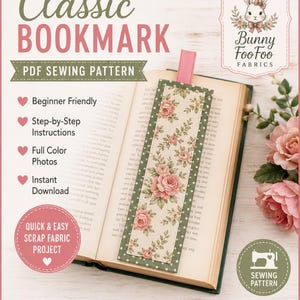 May include: A rectangular fabric bookmark with a floral pattern of pink roses and green leaves on a cream background, bordered by dark green fabric with white dots. A pink ribbon tab extends from the top, resting on an open book page.