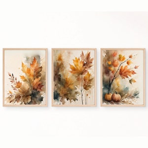 Puede incluir: Conjunto de tres láminas enmarcadas en acuarela con hojas de otoño en tonos naranja, amarillo y marrón. La obra incluye hojas de arce y calabazas, con un fondo neutro y marcos de madera. Ideal para la decoración otoñal.