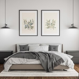May include: A modern bedroom with a bed, two black nightstands, and two framed botanical prints. The bed has a gray headboard, white bedding, and a gray and white patterned throw blanket. Two black pendant lights hang above the bed.