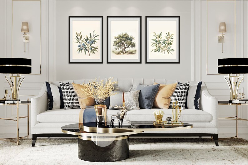 May include: Three framed botanical prints of olive branches and a tree hang above a white sofa with decorative pillows. The room features gold accents, including lamps and side tables, and a black and gold coffee table. The overall style is elegant and classic.