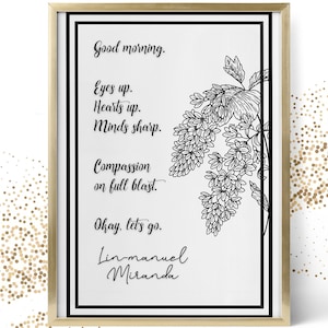 May include: A framed art print with a gold frame, featuring a black and white floral illustration and inspirational text. The text includes phrases like "Good morning," "Eyes up," and "Compassion on full blast," attributed to Lin-Manuel Miranda.