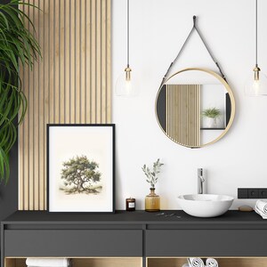 May include: A modern bathroom interior featuring a framed tree art print, a round mirror with a gold frame, and a white sink. The decor includes a large green plant, pendant lights, and wooden accents, creating a serene and stylish space.