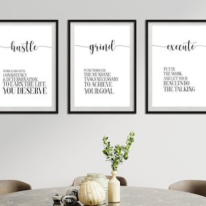 Puede incluir: Tres impresiones artísticas motivacionales enmarcadas con marcos negros. Cada impresión presenta una sola palabra en cursiva: "hustle", "grind" y "execute". Debajo de cada palabra hay una cita inspiradora corta en una fuente limpia y sans-serif. Las impresiones se muestran sobre una mesa.