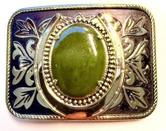 May include: A gold-tone belt buckle with a green stone set in a horseshoe design. The buckle has a black and gold background with floral designs.